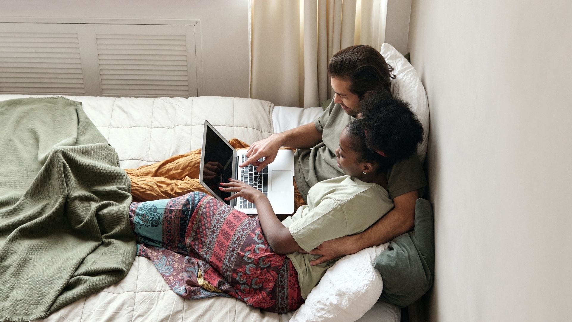 deux personnes dans un lit devant un ordinateur